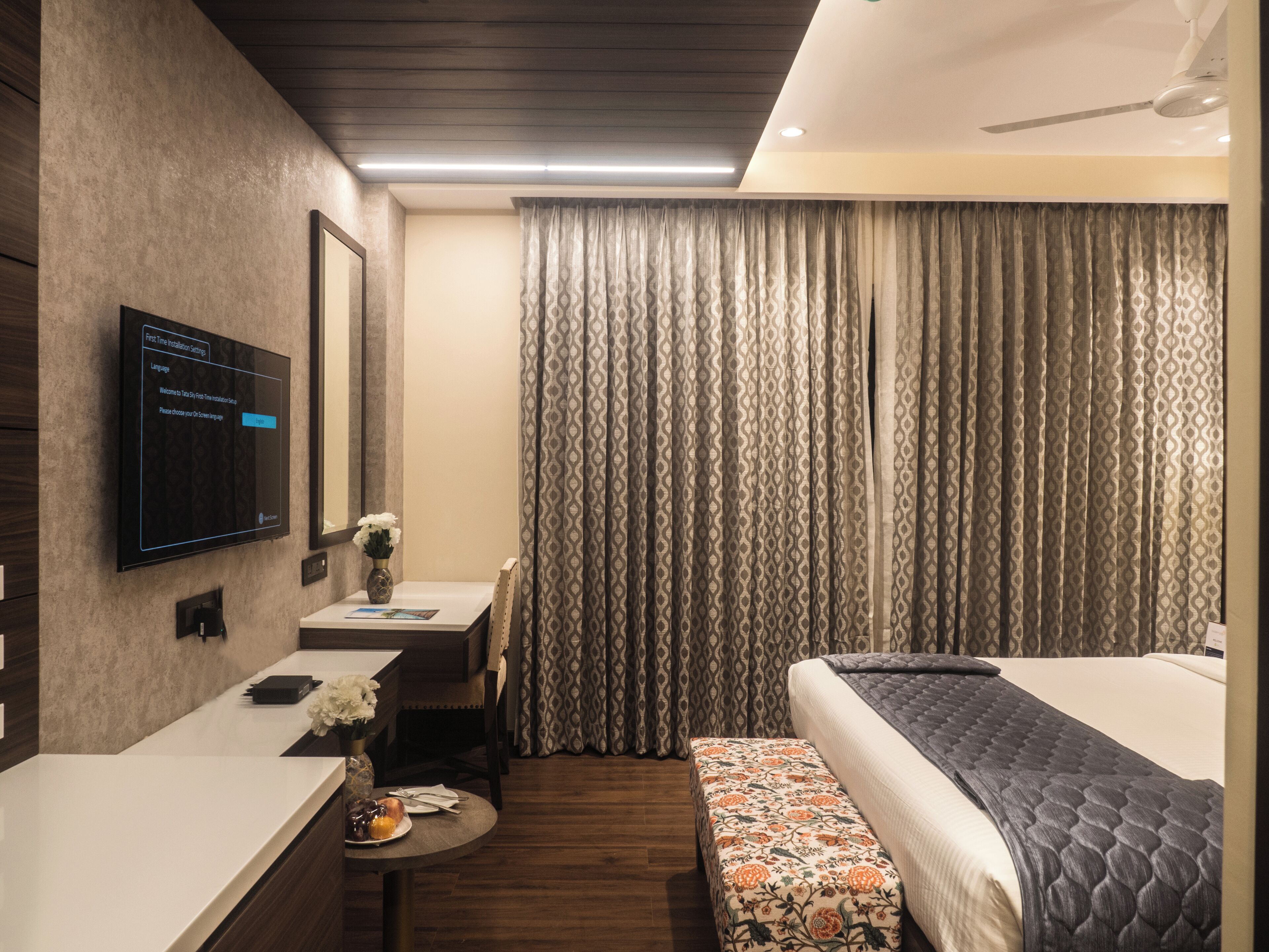 Une chambre d’hôtel comprenant un lit, un bureau avec une chaise, un téléviseur fixé au mur et une fenêtre avec des rideaux.