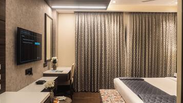A hotel room with a bed, a desk with a chair, a TV mounted on the wall, and a window with curtains.