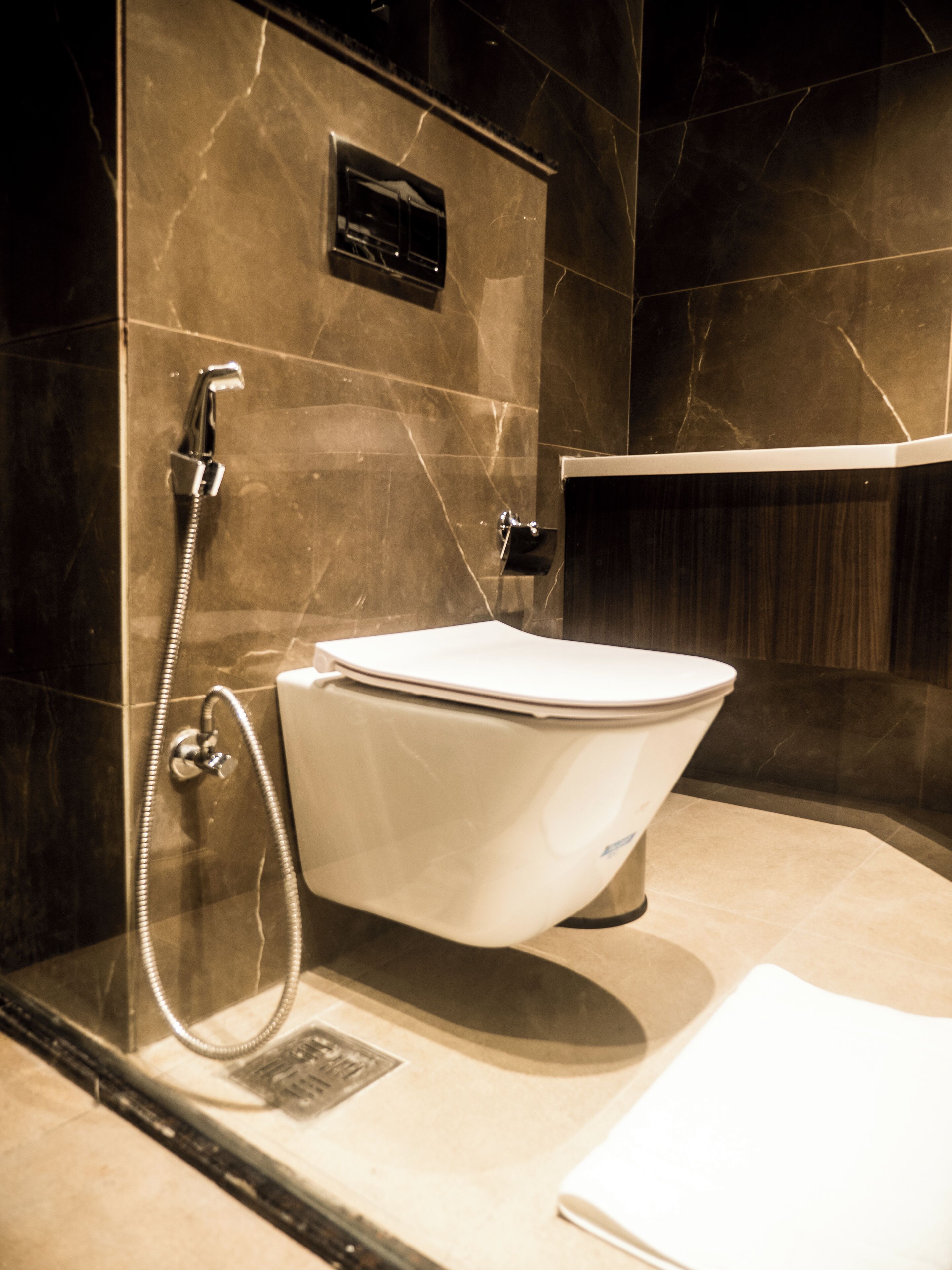 A modern bathroom with a freestanding toilet, a shower with a handheld hose, and a marble-tiled wall.