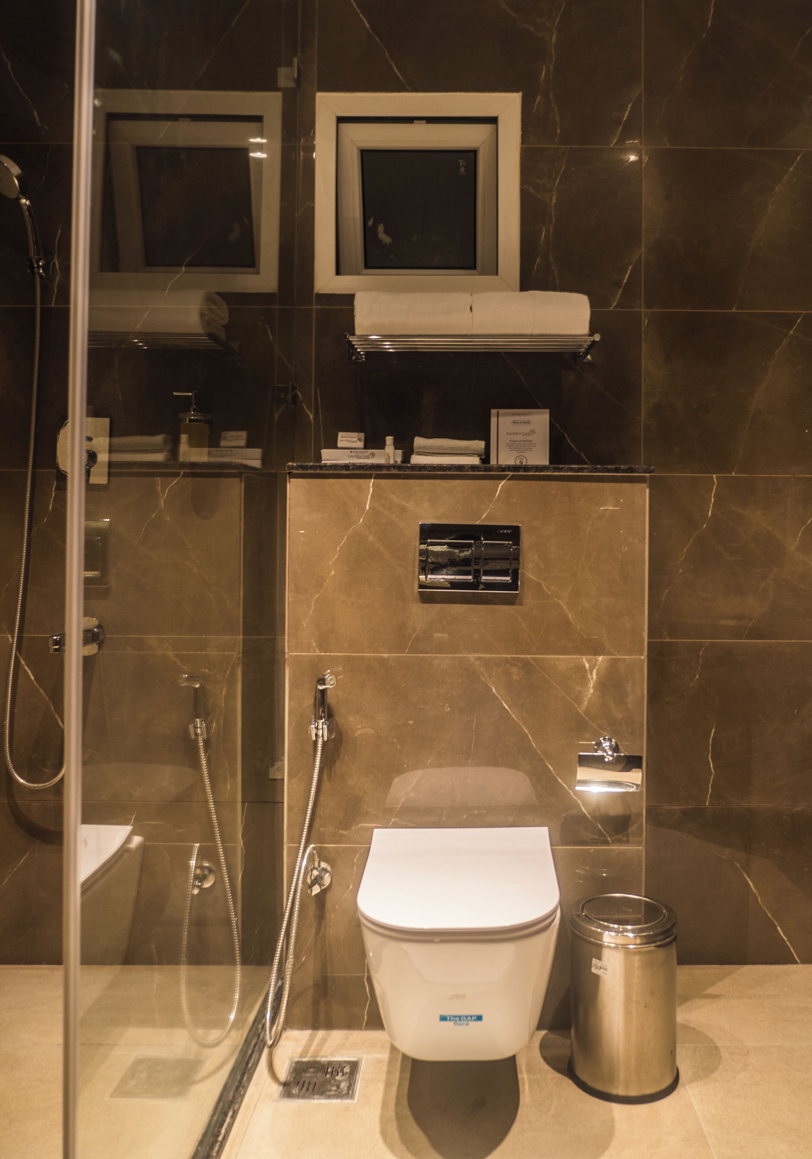 A modern bathroom with a glass-enclosed shower, a toilet, and a trash can.
