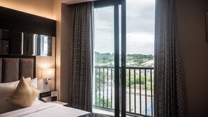 Ein Hotelzimmer mit einem großen Bett, einem Nachttisch mit Lampe, einem Fernseher und Blick auf eine grüne Landschaft vom Balkon aus.