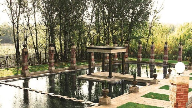 Ein ruhiger Garten mit einem zentralen Teich, einem Gazebo und einer Ziegelmauer.