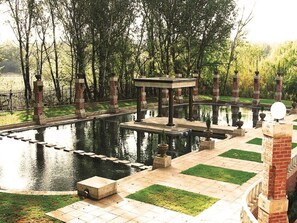 Un jardín tranquilo con un estanque central, un pabellón y un muro de ladrillo.