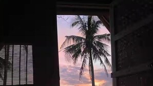 Ein Zimmer mit Bett, Fenster und Blick auf einen Sonnenuntergang über dem Meer.