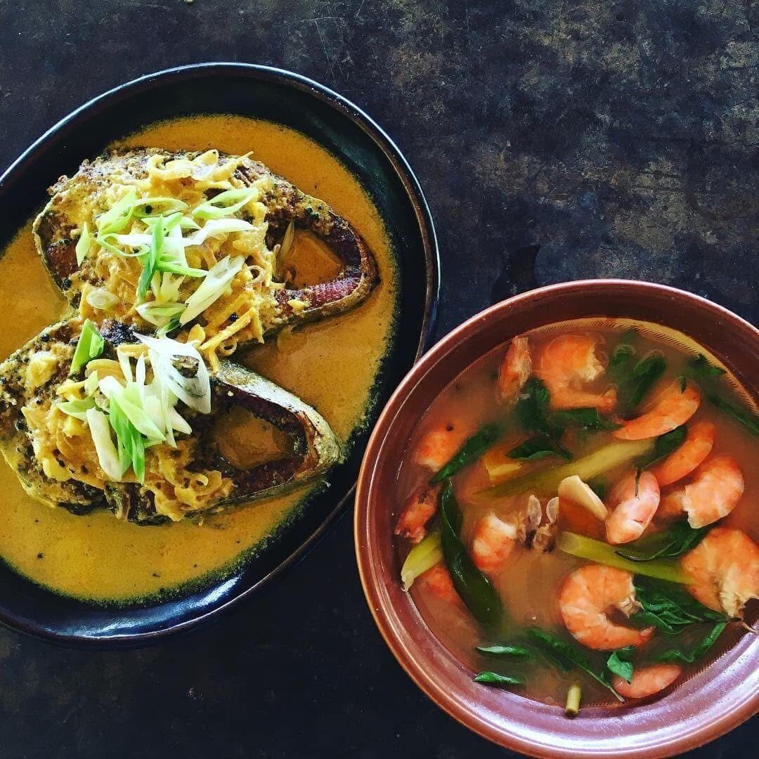A bowl of soup with shrimp and greens, and a plate with grilled fish topped with herbs.