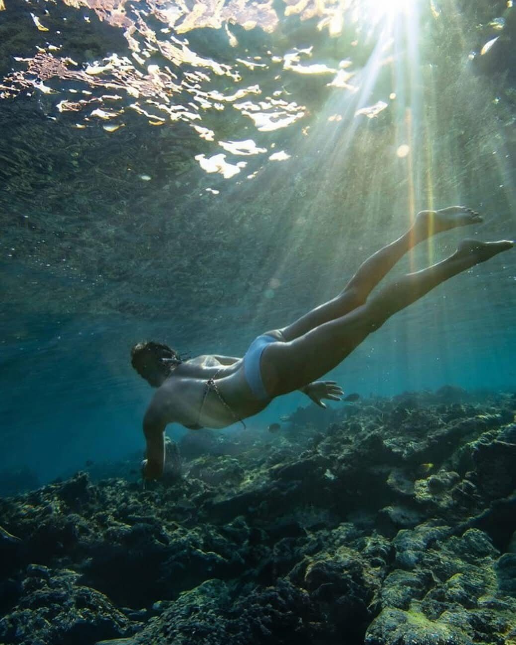 A person swimming underwater with sunlight filtering through the water.