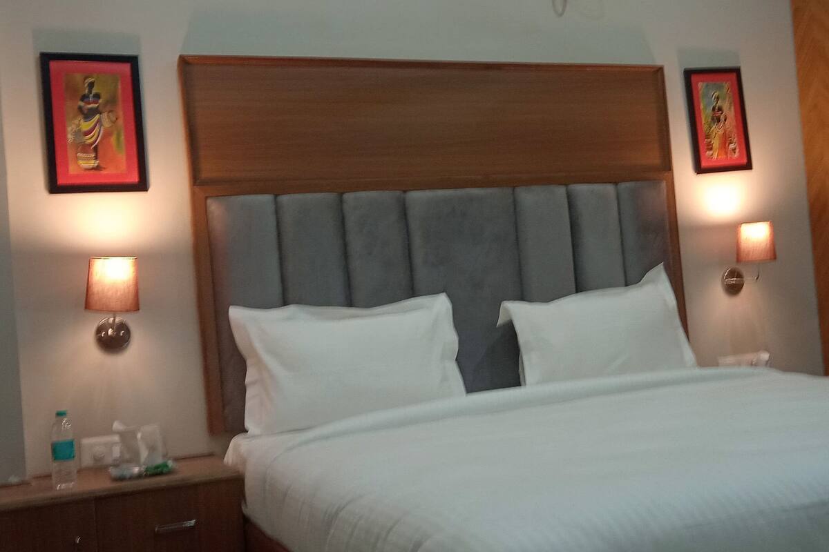 A hotel room with a bed, nightstands, framed artwork, and a wardrobe.