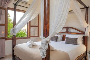 Ein Himmelbett mit Holzrahmen, weißer Bettwäsche und Blick auf Grün.