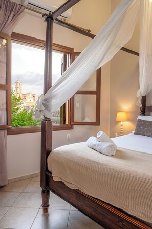 Ein Schlafzimmer mit einem hölzernen Bett, einem Baldachin, Blick auf ein Gebäude mit einem Glockenturm und einer Lampe auf dem Nachttisch.