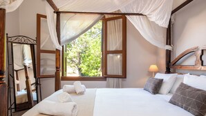 Un lit à baldaquin avec du linge de lit et des oreillers blancs, une tête de lit en bois et une fenêtre avec des rideaux.
