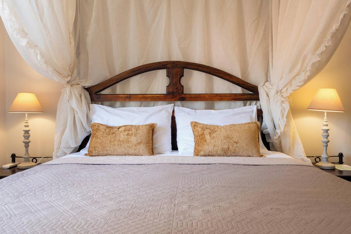 Una cama con dosel, dos lámparas de noche y dos almohadas.