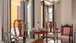 Une pièce avec une table en bois dressée pour deux personnes, deux chaises rembourrées, un fauteuil décoratif et une vue à travers une porte vitrée.