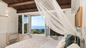 Une chambre à coucher avec un lit, une lampe de chevet, une fenêtre donnant sur la mer et un ventilateur de plafond.