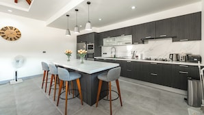 A modern kitchen with dark cabinets, a marble countertop, and a central island with bar stools. - Super modern Brand new Beautiful V162 (Rawai)