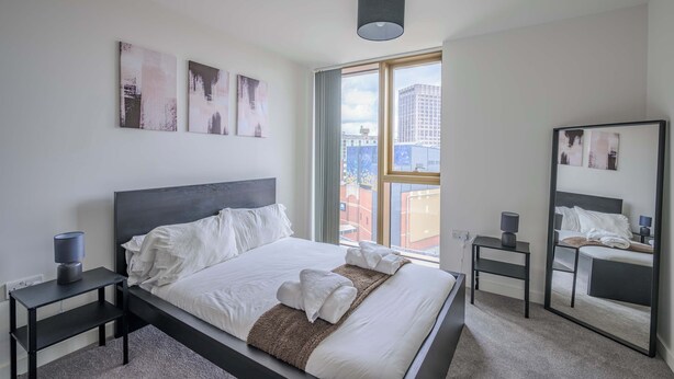 Una habitación de hotel moderna con una cama grande, una mesita de noche con lámpara, un espejo y obras de arte en las paredes.