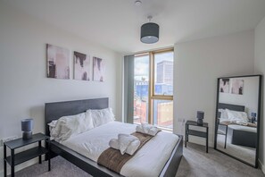 Ein modernes Hotelzimmer mit einem großen Bett, einem Nachttisch mit Lampe, einem Spiegel und Bildern an den Wänden.