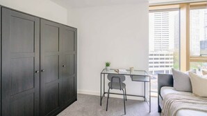Ein Schlafzimmer mit einem Bett, einem Schreibtisch, einem Stuhl, einem Kleiderschrank und einem Fenster mit Blick auf die Stadt.