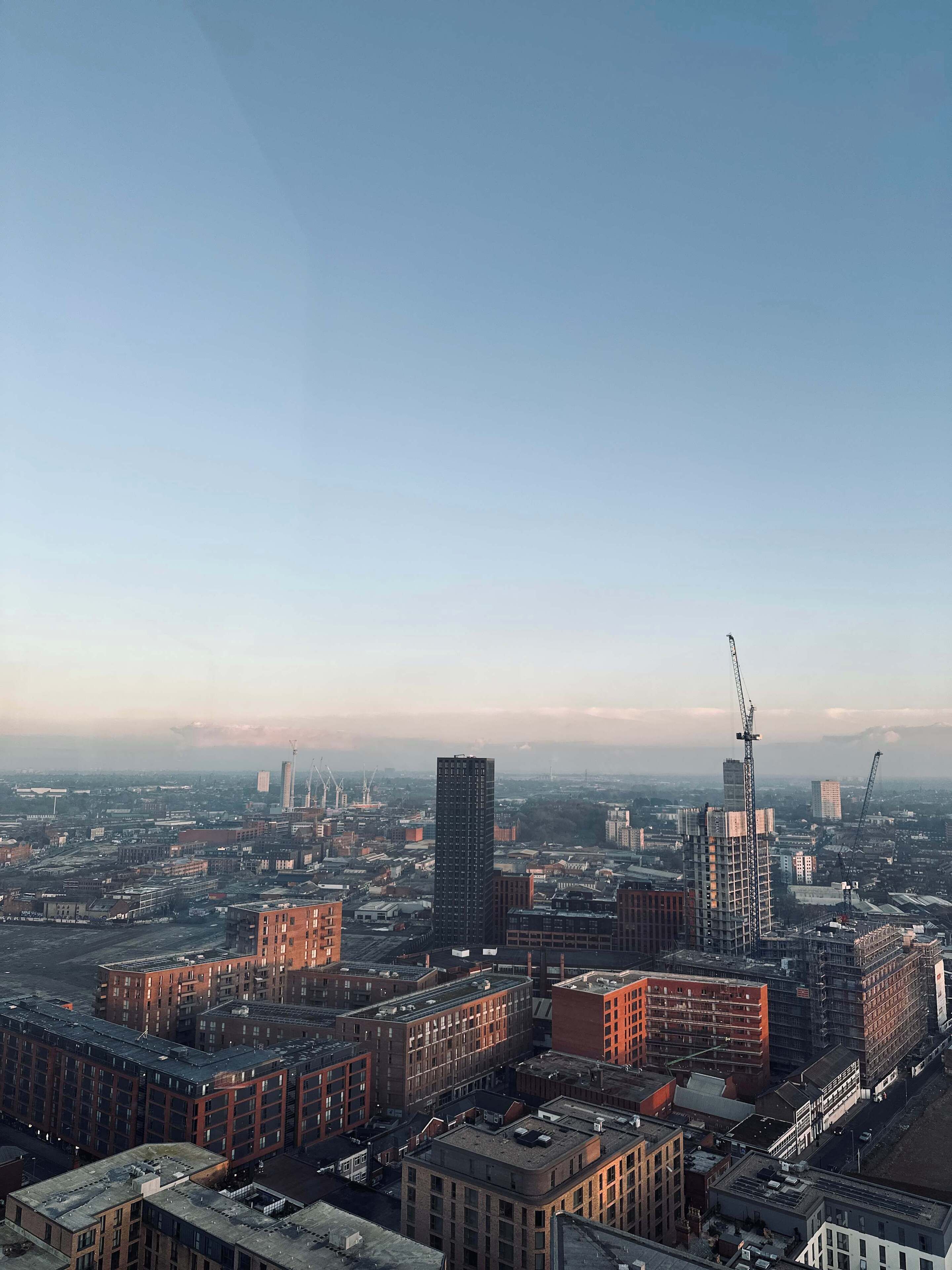 Une vue urbaine comprenant divers bâtiments, notamment un gratte-ciel imposant en construction et plusieurs bâtiments plus anciens en briques.