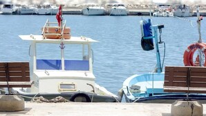 A table set for a meal with various dishes, including bread, olives, and fruits, at a waterfront location with boats in the background. - Sylvana Hotel (Ayvacik)