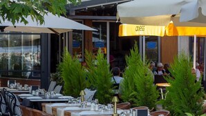 An outdoor dining area with multiple tables and chairs, some covered by umbrellas, and potted plants. - Sylvana Hotel (Ayvacik)