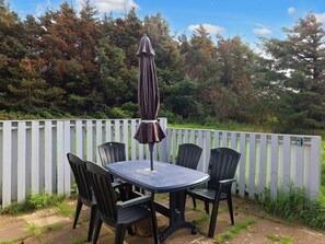 An outdoor patio with a table and four chairs, a brown umbrella, and a white picket fence. - 6 Person Holiday Home in Lokken (Lokken)