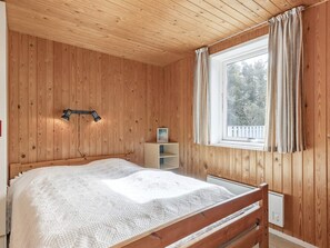 Une chambre à coucher aux murs lambrissés, avec un lit, une table de chevet, une lampe et une fenêtre avec des rideaux.