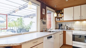 Eine Küche mit Geschirrspüler, Herd und Kaffeemaschine. Ein Fenster bietet Blick ins Freie.