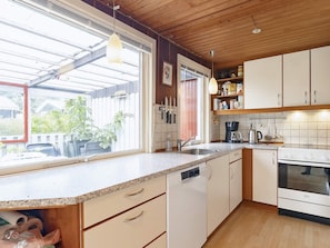 A kitchen with a dishwasher, stove, and coffee maker. There is a window with a view of the outside. - 6 Person Holiday Home in Lokken (Lokken)