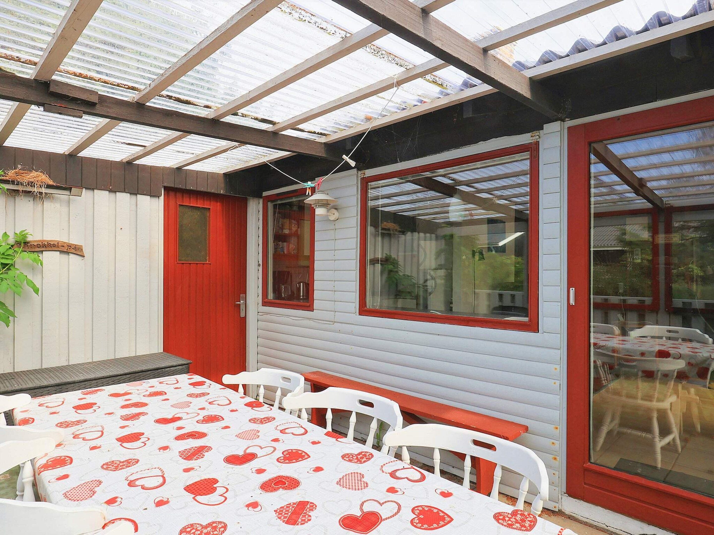 Une terrasse couverte avec une table et des chaises, une porte rouge et une fenêtre donnant sur un beau paysage.