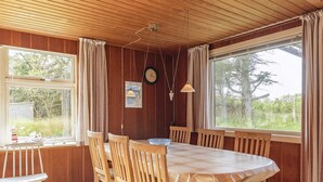 Ein Essbereich mit Holztisch und -stühlen, großen Fenstern mit Vorhängen und einer Uhr an der Wand.