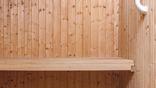 Un sauna en bois avec un banc et un tuyau blanc.