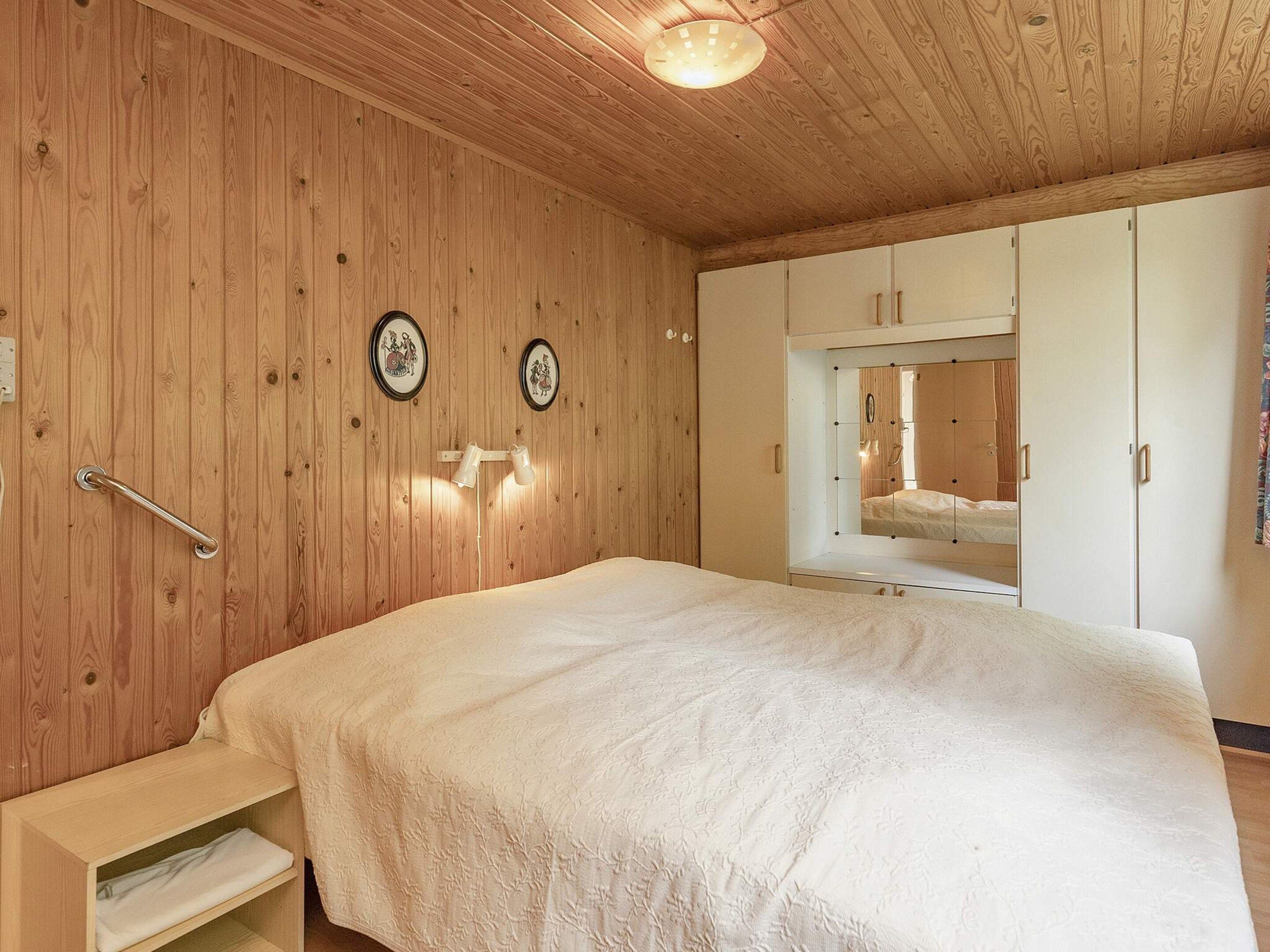 Une chambre avec des murs en bois, un lit, une table de chevet et une armoire.