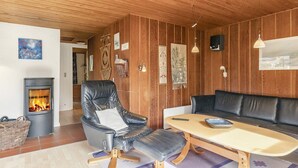Ein gemütliches Zimmer mit Kamin, Ledersessel, Holztisch und einer Couch.