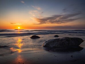 Une plage avec des rochers et l’océan au coucher du soleil.