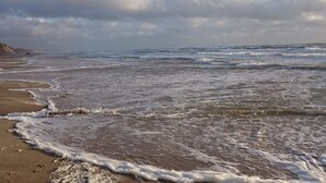 Une plage avec des vagues, un ciel dégagé et des nuages.