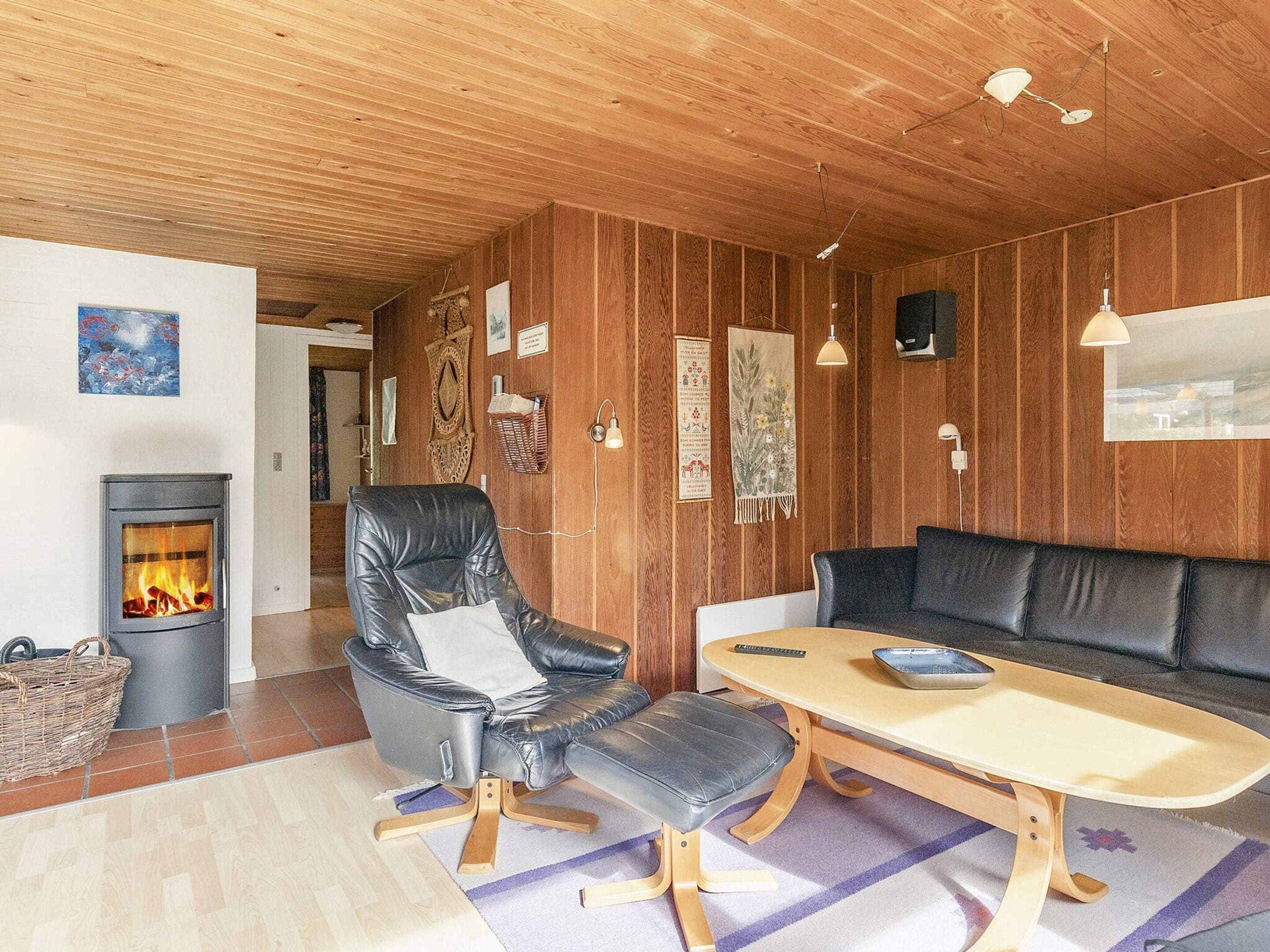 Een gezellige kamer met een open haard, lederen fauteuil, houten tafel en een bank.