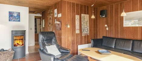 Een gezellige kamer met een open haard, lederen fauteuil, houten tafel en een bank.