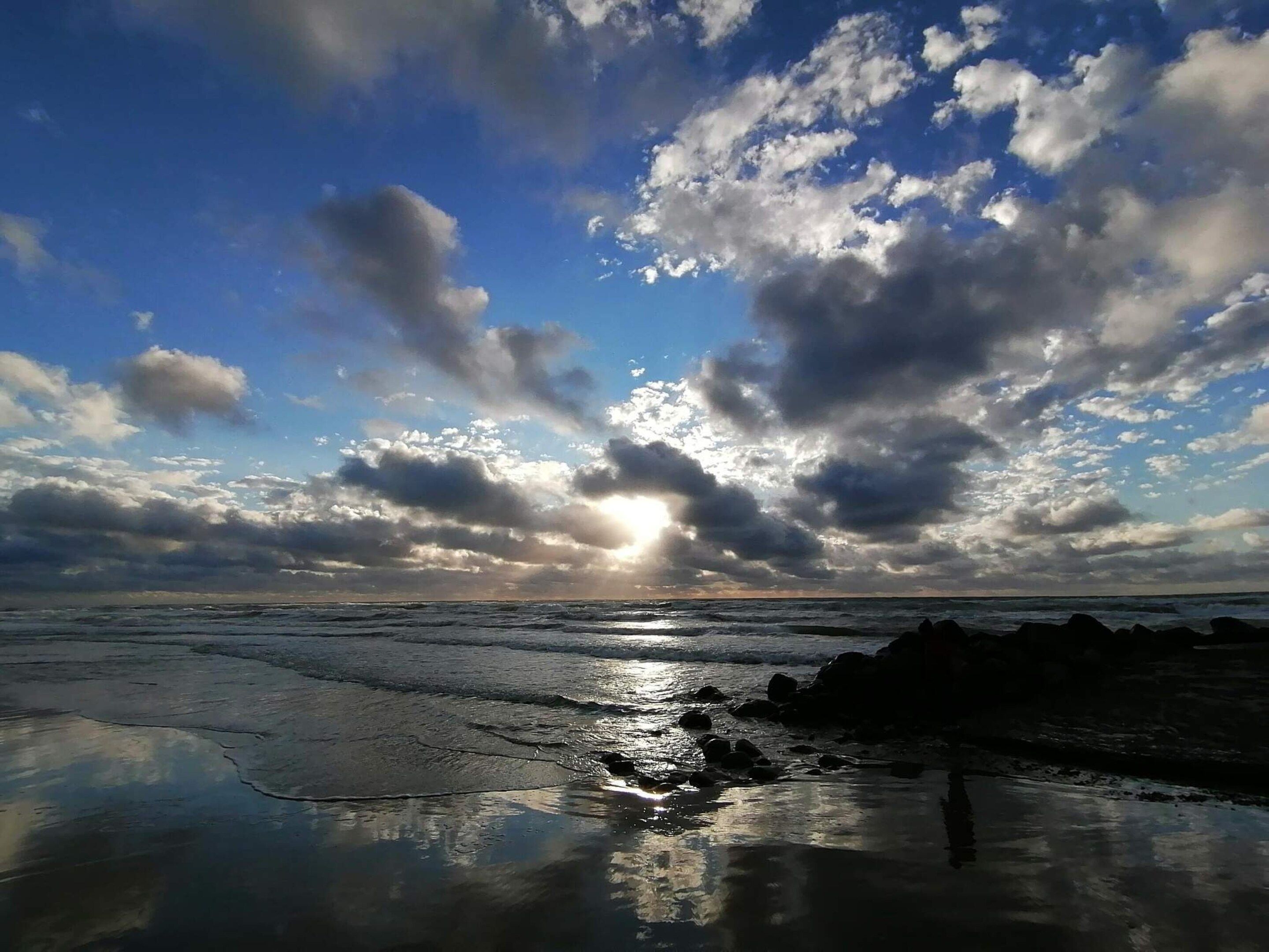 Une plage avec des vagues, des rochers et un ciel nuageux.