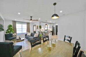 Ein modernes Wohnzimmer mit Essbereich, einer dahinterliegenden Küche und einem Deckenventilator.