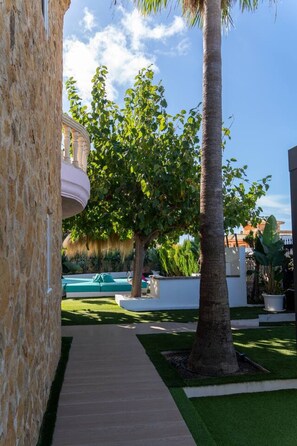 A pathway leading to a pool area with a palm tree and a stone wall. - Villa flamingo súper lujo (Llucmajor)