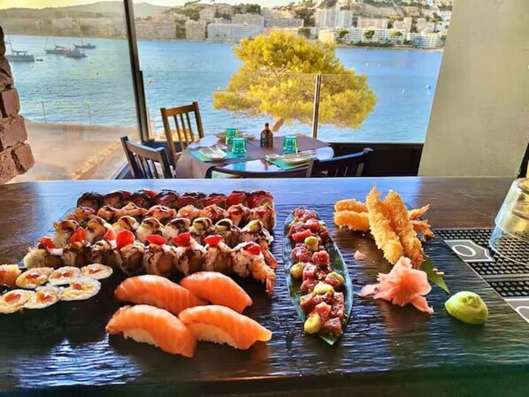 A sushi platter with various types of sushi on a table, with a view of a harbor and buildings in the background.