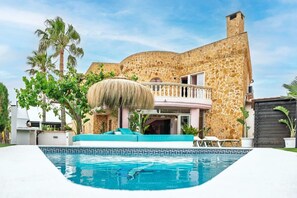 Edifici de pedra amb piscina, teulada de palla i un balcó.