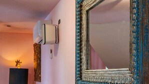 A room with a large mirror, a wooden side table with bottles, a giraffe sculpture, and a wall-mounted air conditioner.