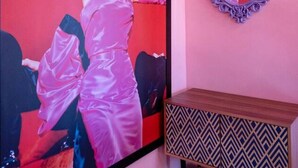 A room with a large framed picture of a person in a pink dress, a mirror with an ornate frame, and a patterned wooden cabinet.