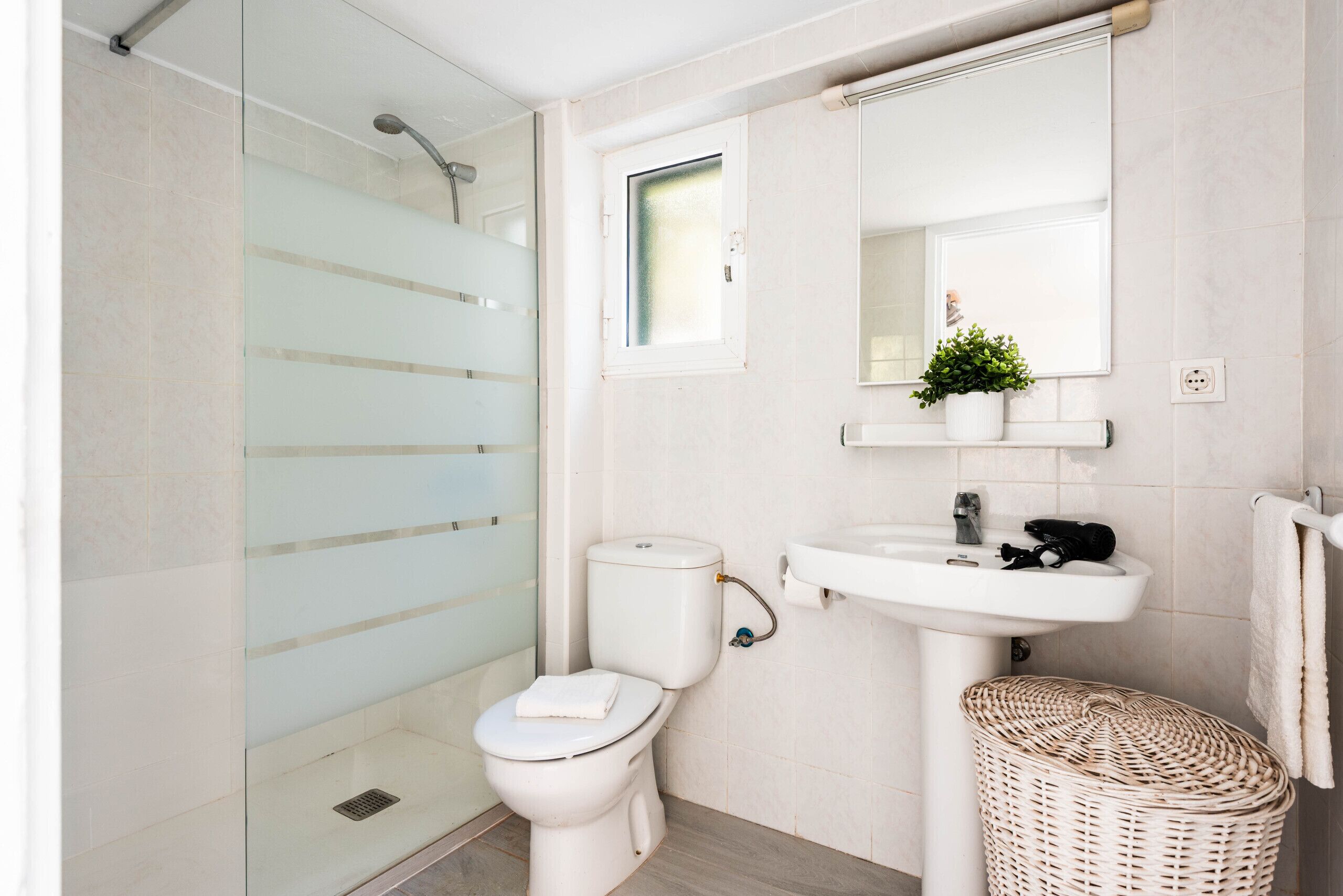 A bathroom with a glass shower enclosure, a toilet, a sink, and a wicker basket.