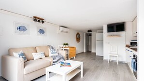 Una sala de estar moderna con un sofá color beige, una mesa de centro blanca y un comedor con una mesa y sillas de madera.