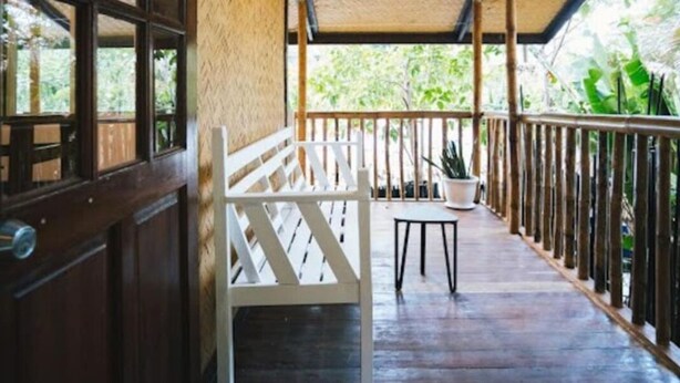 A wooden porch with a white bench, a small table, and a potted plant.
