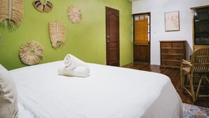 A room with a bed, a wooden door, a wicker chair, and wall decorations.
