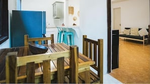 A dining area with a wooden table and chairs, a blue refrigerator, and a kitchen in the background.