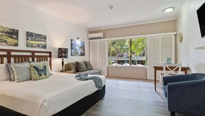 A bedroom with a bed, a sofa, a desk, and a window with a view of greenery. - Charming studio with WiFi, fitness room in delightful Port Douglas. (Port Douglas)